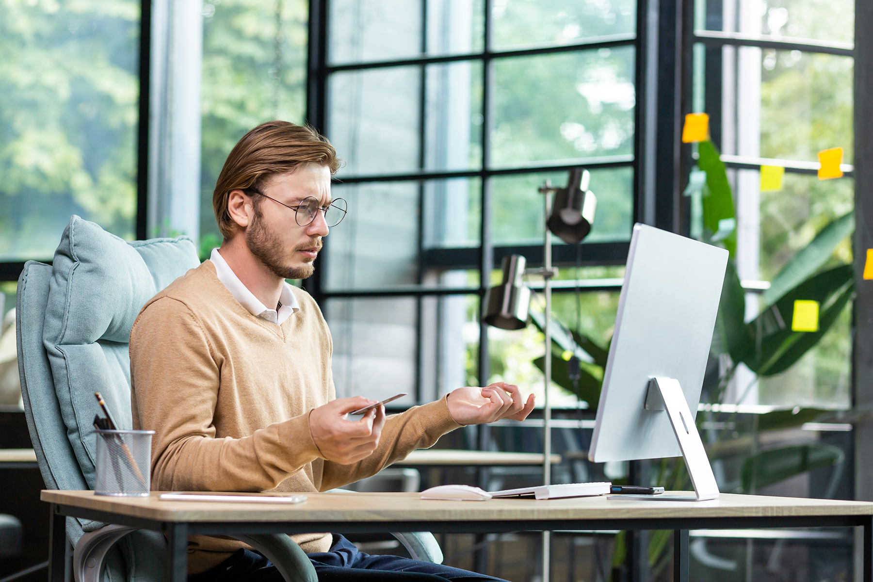 Financial problems. A young male businessman is sitting at a desk in the office and looking worriedly at the computer and holding a credit problem