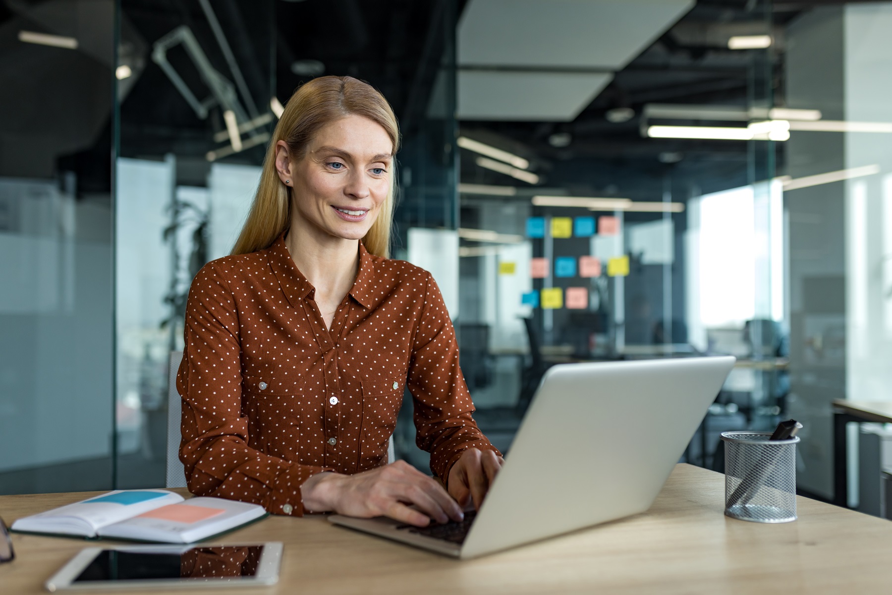 Mature businesswoman using a laptop in a modern office setting with focus on productivity and planning while engaging in her professional tasks, showcasing leadership and technology use L'Impact de l'Éclairage sur la Productivité au Bureau